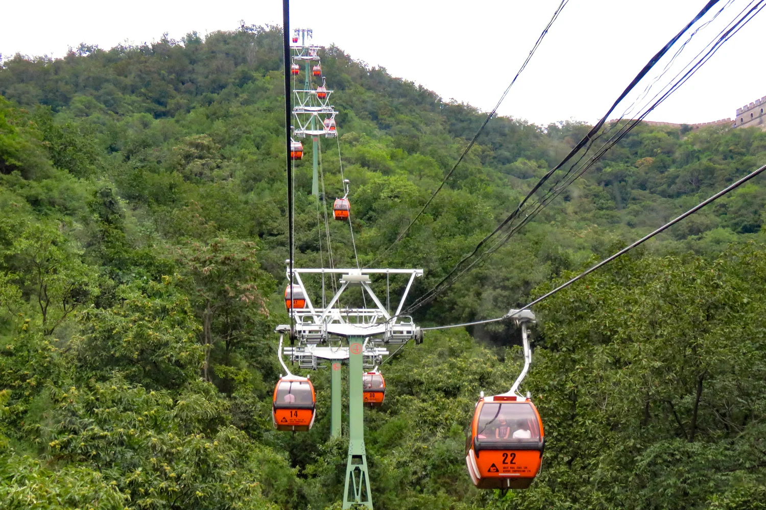 Orange enclosed cable-car cabins above wooded hills